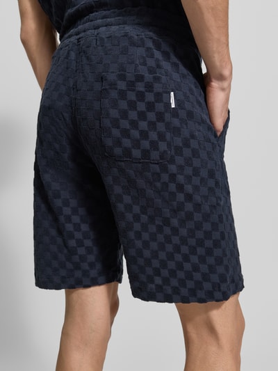Männermodel trägt Regular Fit Shorts mit Label-Patch von Lindbergh aus dunkelblauem Baumwoll-Mix mit Eingrifftaschen und Gesäßtasche, Ganzkörperansicht Rückansicht.