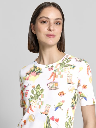 Frauenmodel trägt Damen T-Shirt im Allover-Look von Marc Cain aus Baumwoll-Elasthan-Mix, Slim-Fit, mit Rundhalsausschnitt, Nahaufnahme Oberkörper. Rückenlänge 55 cm bei Größe 36, bunte Motive auf weißem Grund, glatte Textur.