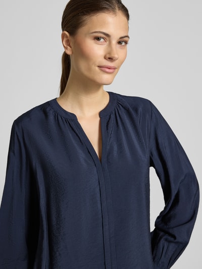 Vrouwenmodel draagt Relaxed Fit Langarmbluse aus Viskose-Mix van s.Oliver RED LABEL in donkerblauw met tuniekkraag, V-hals en afgeronde rompzoom, materiaal viscosemix, naaddetails, Nahaufnahme Oberkörper.