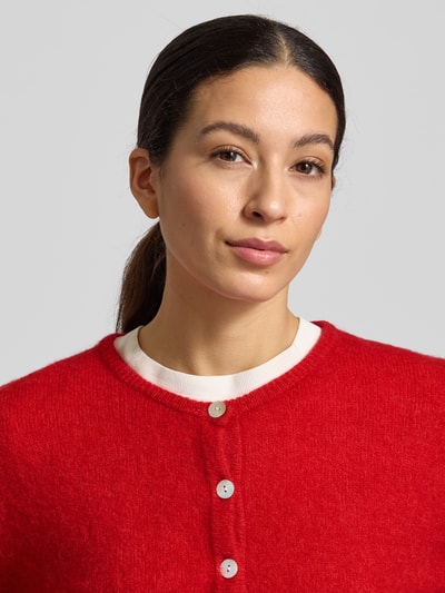 Frauenmodel trägt Strickjacke mit Knopfleiste Modell 'VITOW' von American Vintage in Rot, Alpaka-Lanawoll-Mix, Nahaufnahme Oberkörper.