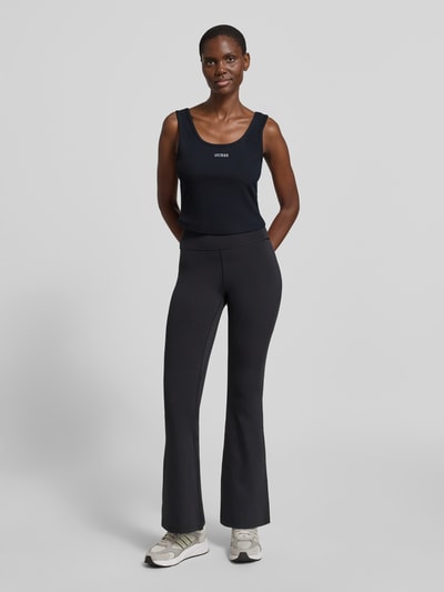 Frauenmodel trägt Slim Fit Top mit Logo-Stitching Modell 'Circe' von Guess, schwarzer Ton, runder Ausschnitt, elastischer Baumwollmix, Ganzkörperansicht von vorne.