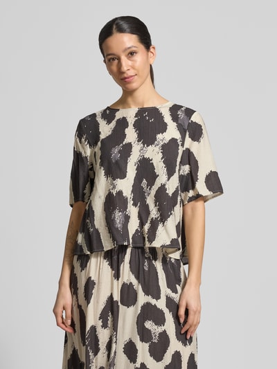 Frauenmodel trägt Blusenshirt aus Viskose-Mix Modell 'Karalie Jusia' von MSCH Copenhagen, gerader Schnitt, Rundhalsausschnitt, Halbarm, cremefarben mit schwarzen abstrakten Punkten, glatte Textur, Nahaufnahme Oberkörper.