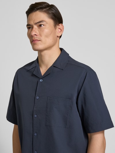 Männermodel trägt Relaxed Fit Freizeithemd mit Seersucker-Verarbeitung Modell 'LAPISY_M' von BOSS Orange in Dunkelblau, Nahaufnahme Oberkörper. Unifarbenes Herrenhemd mit Resortkragen, kurzer Knopfleiste, Brusttasche, Label Stitching und Seitenschlitzen.