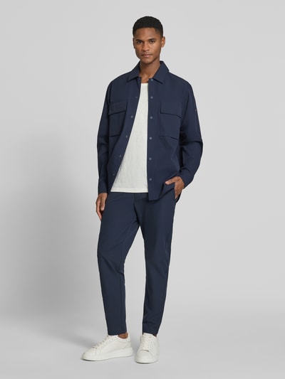 Männermodel trägt Tapered Chino mit Tunnelzug von BOSS Orange in Dunkelblau, unifarben, mit seitlichen Taschen, Ganzkörperansicht von vorne.