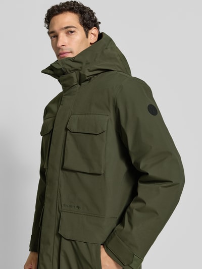 Männermodel trägt Parka mit Kapuze und Pattentaschen Modell 'AIDEN' von Didriksons in Olivgrün, Regular Fit, Nahaufnahme Oberkörper. Rückenlänge 95 cm, Schulterbreite 47 cm, Brustweite 55 cm, Ärmellänge 68 cm.