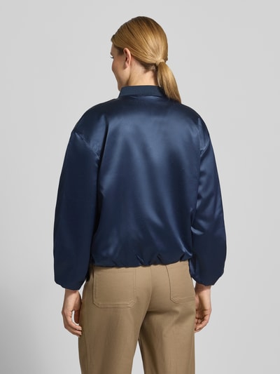 Modelka nosi Regular Fit Blouson mit College-Kragen von Tom Tailor, efekt: jednolity kolor, krój regular fit, kołnierz college, zamek błyskawiczny, długi rękaw, elastyczne wykończenie, wpuszczane kieszenie, wykończenie materiału: satyna; widok całej sylwetki z tyłu.