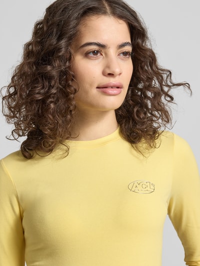 Frauenmodel trägt Slim Fit Longsleeve mit Logo-Detail von ANOTHER COTTON LAB in Hellgelb, elastischer Baumwoll-Mix, Nahaufnahme Oberkörper.