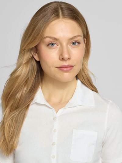 Modelka kobieca nosi Regular Fit Poloshirt aus reiner Baumwolle von Marc O'Polo, efekt: jednolity kolor, krój regular fit, nadruk z logo, kołnierzyk polo, listwa guzikowa krótka, krótki rękaw, brustasza, wykończenie materiału: dżersej, materiał: bawełna, zbliżenie na górną część ciała.
