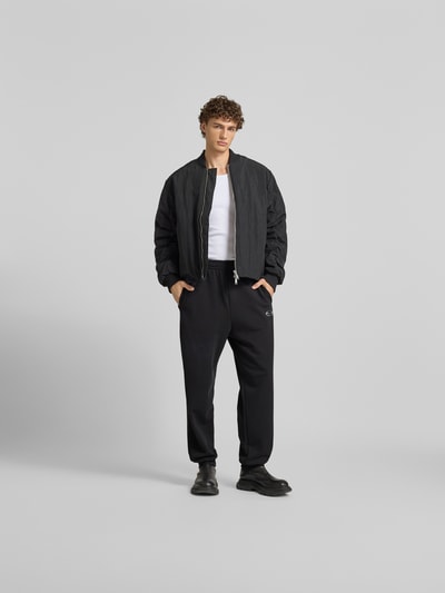 Männermodel trägt schwarze Sweatpants mit Label-Detail von Diesel aus reiner Baumwolle, lockerer Schnitt, elastischer Bund, Gesäßtasche, Innenbeinlänge 71 cm, Bundweite 42 cm, Ganzkörperansicht von vorne.