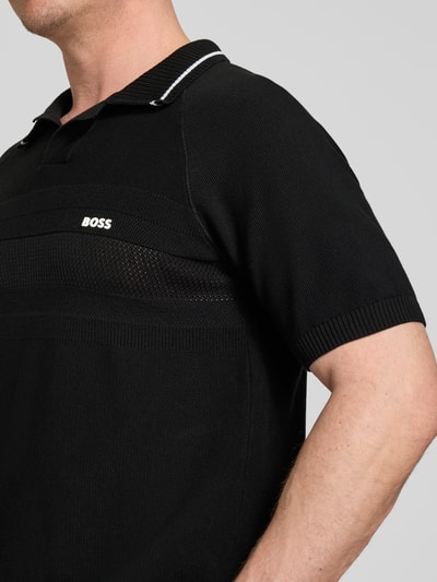 Männermodel trägt Regular Fit Poloshirt aus Strick von BOSS Green in Schwarz, Strickoptik, Polokragen, Kurzarm, reine Baumwolle, Nahaufnahme Oberkörper.