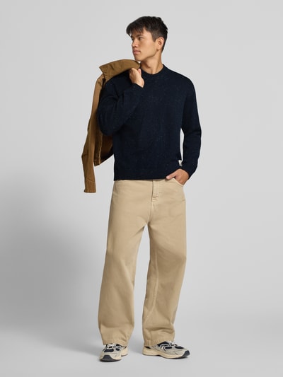 Männermodel trägt Regular Fit Strickpullover mit Rundhalsausschnitt von JACK & JONES in Dunkelblau, beiger Hose, Vorderansicht, Baumwoll-Mix, gerippte Abschlüsse, lange Ärmel, Logo-Patch, Kontext: Rückenlänge 66 cm, Ärmellänge 64 cm, Ganzkörperansicht von vorne.