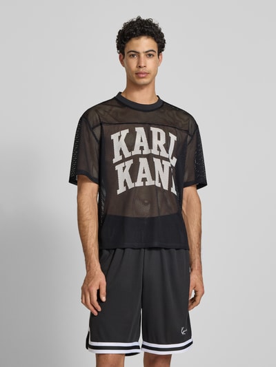 Männermodel trägt Oversized T-Shirt mit Logo-Print von KARL KANI aus schwarzem Mesh, Oversized-Fit, Rundhalsausschnitt, Herren T-Shirt, Rückenlänge bei Größe M 66 cm, Ganzkörperansicht von vorne.