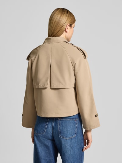 Modelka nosi Boxy Fit Trenchcoat mit doppelreihiger Knopfleiste Modell 'CHLOE' von Vero Moda w jednolitym beżu, długi raglanowy rękaw, umlegekragen, gun flap, kieszenie boczne, regulowane mankiety, detal z kontrafałdą, widok całej sylwetki od tyłu.
