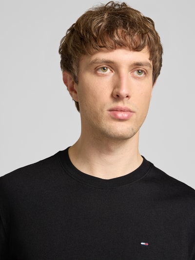 Männermodel trägt Regular Fit T-Shirt aus reiner Baumwolle von Tommy Jeans, Optik: Unifarben, Logo-Stitching, Nahaufnahme Oberkörper.
