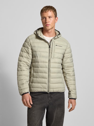 Männermodel draagt Gewatteerd jack met capuchon en logoprint van CHAMPION, regular fit, ritssluiting, steekzakken, kleur lichtgrijs, Ganzkörperansicht von vorne. Ruglengte maat M: 71 cm, schouderbreedte: 51 cm, borstwijdte: 61 cm, mouwlengte: 69 cm.