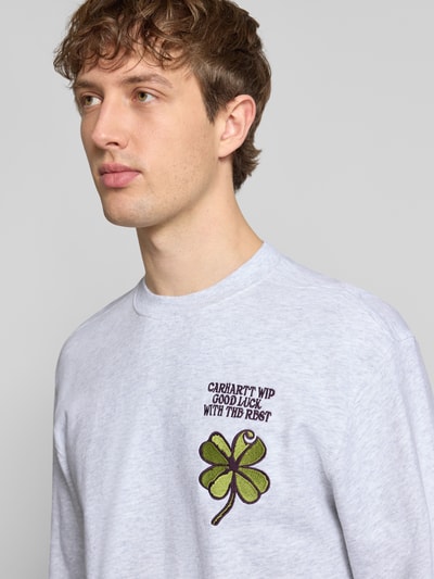 Mężczyzna nosi Sweatshirt mit Label-Detail od Carhartt Work In Progress, bawełna, krój regular fit, jasnoszary, detal z przodu, zbliżenie na górną część ciała.