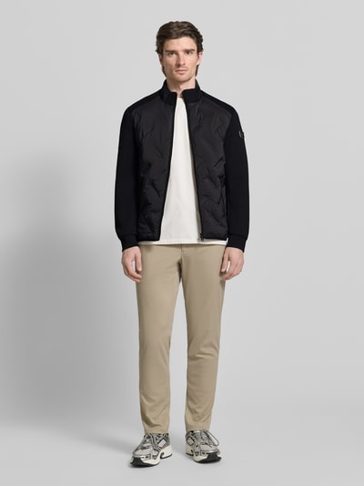 Männermodel trägt Regular Fit Jacke mit Stehkragen von Guess in Schwarz mit Reißverschluss und Eingrifftaschen, Ganzkörperansicht von vorne.