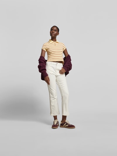 Frauenmodel trägt Cropped Poloshirt aus reiner Baumwolle von Rabanne, gestreift in Beige und Gelb, Polokragen, verlängerte Rückseite, kurzärmelig, Rückenlänge bei Größe S 47 cm, Ganzkörperansicht von vorne.
