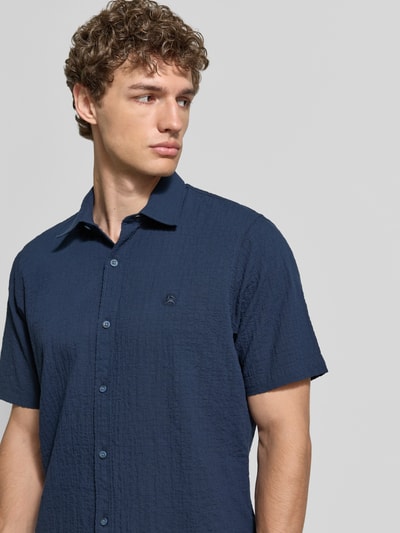 Männermodel trägt Relaxed Fit Freizeithemd mit Logo-Stitching und Kentkragen von Lerros in dunkelblauem Seersucker, Nahaufnahme Oberkörper. Rückenlänge bei Größe M 75 cm, Schulterbreite 45 cm, Ärmellänge 25 cm, Knopfleiste, abgerundeter Saum.