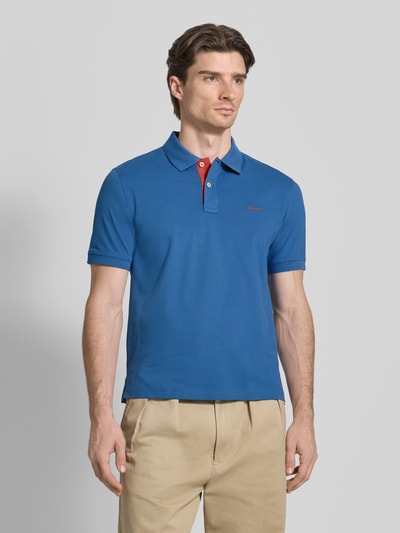 Männermodel trägt Regular Fit Poloshirt mit Logo-Stitching von Gant in Blau, Polokragen, Kurzarm, aus elastischem Baumwoll-Mix, Ganzkörperansicht von vorne.