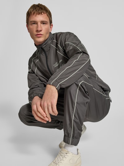 Männermodel trägt Trainingsjacke mit Reißverschlusstaschen von HALO, Regular Fit, Stehkragen, Label-Print, Grau, Ganzkörperansicht von vorne.