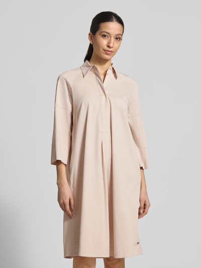 Frauenmodel trägt Hemdblusenkleid mit Viskose-Anteil von Marc Cain in Beige, gerader Schnitt, Hemdblusenkragen, verdeckte Knopfleiste, 3/4-Arm, überschnittene Schultern, Label-Detail, glatte Stofftextur, Rückenlänge bei Größe 36: 101 cm, Brustweite: 53 cm, Ärmellänge: 48 cm, Ganzkörperansicht von vorne.