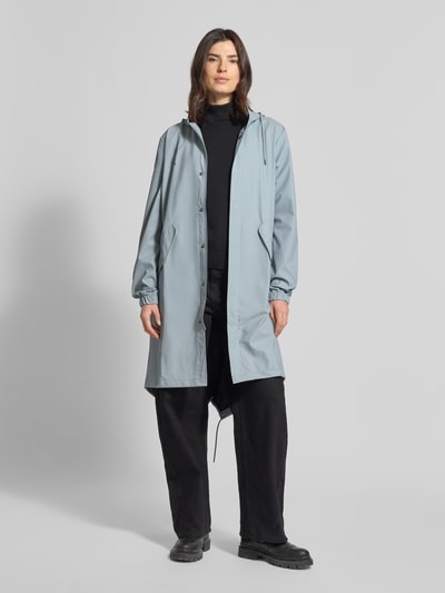 Frauenmodel trägt Regular Fit Parker mit Kapuze Modell 'Fishtail' von Rains in Hellblau, mit Pattentaschen und elastischen Ärmelabschlüssen, Ganzkörperansicht von vorne. Rückenlänge bei Größe S: 104 cm, Schulterbreite: 45 cm, Brustweite: 55 cm, Ärmellänge: 65 cm.
