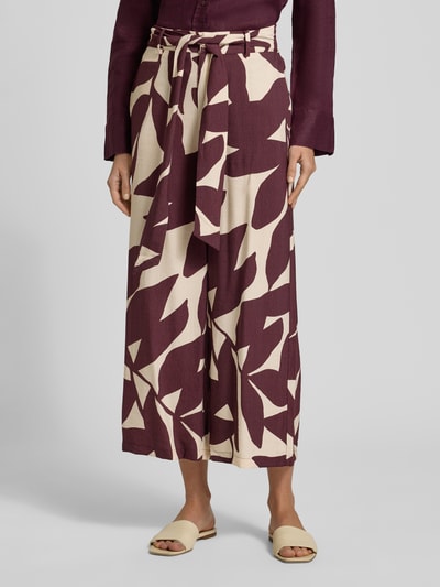 Frauenmodel trägt Stoffhose aus Viskose-Mix mit Bindegürtel Modell 'PLUMAS' von Mango, Allover-Look in Creme und Bordeaux, Nahaufnahme Unterkörper.