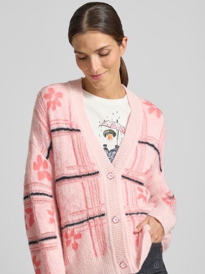 Frauenmodel trägt Oversized Cardigan mit Alpaka-Mohair-Anteil von Marc Cain, rosa mit floralen Mustern, Nahaufnahme Oberkörper.