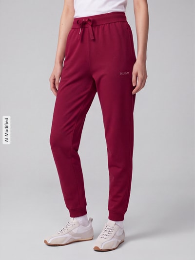 Vrouwenmodel draagt Regular Fit Jogpant aus Baumwoll-Mix Modell 'Hugo ID Pant' van HUGO, dames jogpant, bordeauxrood, gladde textuur, volledige lichaamsvoorzijde, KI-modified beeld