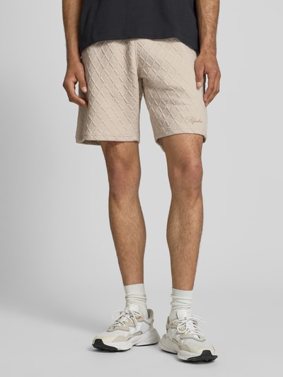 Männermodel trägt Relaxed Fit Shorts mit Strukturmuster Modell 'Jovren' von Pegador aus Elastischer-Material-Mix mit Baumwoll-Anteil, beige Farbe, sichtbares Strukturmuster, Bundweite bei Größe M 39 cm, Innenbeinlänge 24 cm, Ganzkörperansicht von vorne.