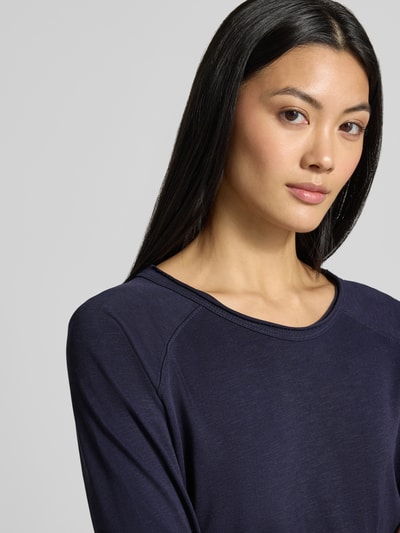 Kobiece model prezentuje bluzkę z długim rękawem 'Longsleeve mit Rundhalsausschnitt' od Smith and Soul z bawełny, luźny krój, jednokolorowy, okrągły dekolt, długość tyłu w rozmiarze S: 61 cm, zbliżenie na górną część ciała.