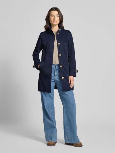 Frauenmodel trägt Trenchcoat mit Stehkragen und Ärmelriegeln von Christian Berg Woman Selection in Dunkelblau, Ganzkörperansicht von vorne. A-Linie, Knopfleiste, kombinierbar zu Jeans, glatte Textur.
