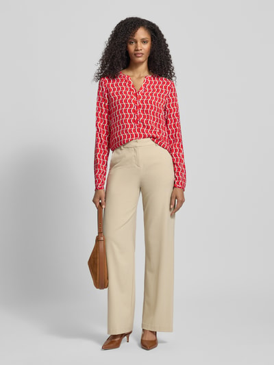 Vrouwenmodel draagt Regular Fit Bluse aus Viskose mit V-Ausschnitt van Christian Berg Woman, rood allover patroon, knoopsluiting, effen beige broek, lange mouwen, voorkant volledige lichaamsweergave.