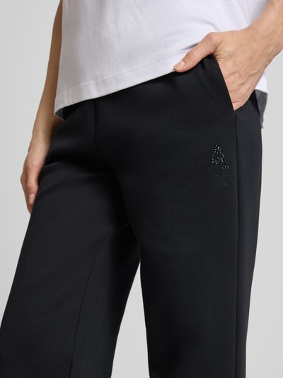 Frauenmodel trägt schwarze Sweatpants mit elastischem Bund und Logo-Print von ARMANI EXCHANGE, seitliche Eingrifftaschen, Nahaufnahme Oberkörper.