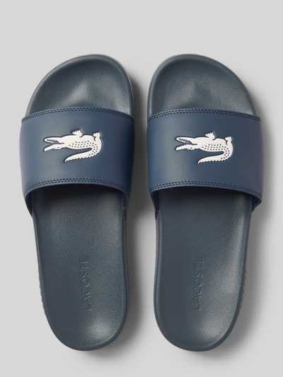Produktfoto, Badeschuhe mit Logo Print Modell 'SERVE SLIDE' von Lacoste für Herren, Optik: Unifarben, Schuhspitze: abgerundet, Absatzform: flach, Applikation: Logo-Print, Verschluss: Schlupf/offen, Sohle: strukturiert, dunkelblaue Farbe, glatte und strukturierte Texturen.