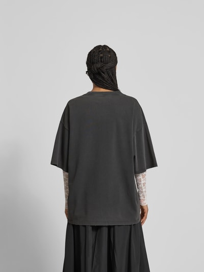 Frauenmodel trägt Oversized T-Shirt mit Label-Stitching von black palms in Dunkelgrau, Reine Baumwolle, Abschlüsse im Destroyed-Look, Rückenlänge 77 cm, Ganzkörperansicht Rückansicht.