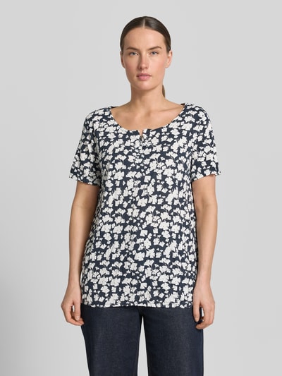 Frauenmodel trägt Regular Fit T-Shirt mit Viskose-Anteil von Tom Tailor, Damen T-Shirt mit weißem Blumenmuster auf dunkelblau, Ganzkörperansicht von vorne.