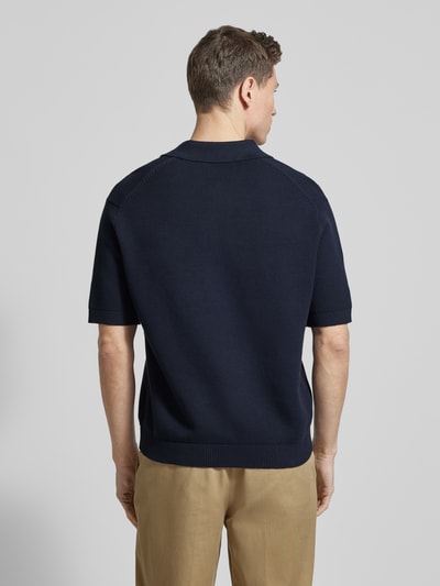 Männermodel trägt Relaxed Fit Poloshirt aus reiner Baumwolle Modell 'DANE' von SELECTED HOMME, dunkelblau, Strickoptik, Ganzkörperansicht Rückansicht.
