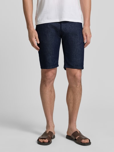 Männermodel trägt Regular Fit Jeansshorts mit Eingrifftaschen Modell 'Sisteron' von Pierre Cardin aus Baumwoll-Elasthan-Mix, Ganzkörperansicht von vorne. Herren Jeansshorts, dunkelblau, glatte Textur, Bundweite 40 cm in Größe 32, Innenbeinlänge 27 cm.