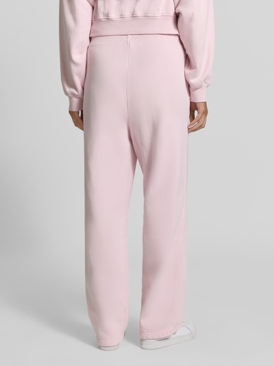 Frauenmodel trägt hellrosa Sweatpants aus reiner Baumwolle mit Logo-Print Modell 'PLIZZY' von American Vintage, elastischer Bund, Straight Fit, Eingrifftaschen, feine strukturierte Textur, Ganzkörperansicht Rückansicht.