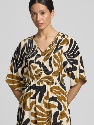 Frauenmodel trägt Damen Midikleid aus Reine Viskose mit Smok-Details Modell 'FELDI' von Soyaconcept, Taillierter Schnitt, V-Ausschnitt, Creme, Braun und Schwarz mit abstraktem Muster, Nahaufnahme Oberkörper. Rückenlänge bei Größe S: 119 cm, Brustweite bei Größe S: 44 cm, Ärmellänge bei Größe S: 25 cm.