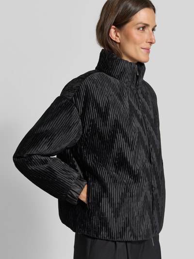Frauenmodel trägt schwarze Jacke mit Zweiwege-Reißverschluss von Emporio Armani, Ripp-Optik, Stehkragen, elastische Ärmelabschlüsse, Ganzkörperansicht von vorne.