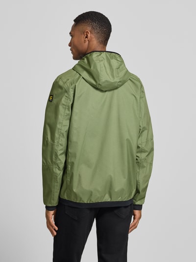 Männermodel trägt grüne Herren Jacke mit Kapuze Modell 'KOS' von Killtec, gerader Schnitt, Label-Patch, Rückenansicht, Ganzkörperansicht Rückansicht.
