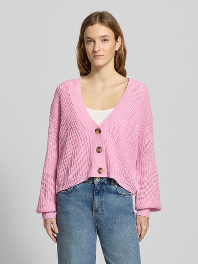 Frauenmodel trägt Regular Fit Strickjacke mit einreihiger Knopfleiste Modell 'CAROL NICE' von Only in Rosa, Strickoptik, unifarben, cropped, langarm, tiefer V-Ausschnitt, gerippte Abschlüsse, Label Stitching, Ganzkörperansicht von vorne.