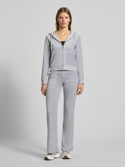 Frauenmodel trägt Low Rise Sweatpants mit elastischem Bund Modell 'LAYLA' von Juicy Couture aus Baumwoll-Mix mit Stretch-Anteil, Flared-Cut, Low-Rise, Eingrifftaschen, grau meliert, glatte Textur, Ganzkörperansicht von vorne.