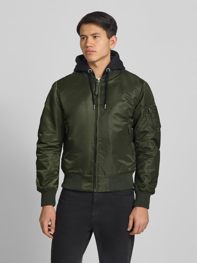 Männermodel trägt Bomberjacke mit Kapuze und Reißverschlusstaschen von Superdry in Olivgrün, Regular-Fit, Ganzkörperansicht von vorne, Rückenlänge bei Größe M 56 cm, Schulterbreite 45 cm, Brustweite 60 cm, Ärmellänge 68 cm.