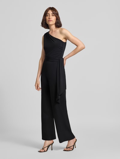 Frauenmodel trägt Jumpsuit mit Stretch-Anteil von Oui in Schwarz, One-Shoulder-Design, tailliert, mit Taillenband, Ganzkörperansicht von vorne.