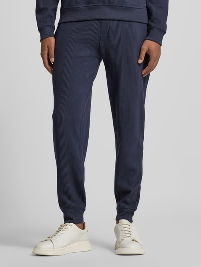 Männermodel trägt Comfort Fit Sweatpants aus Baumwoll-Mix Modell 'STRUCTURE PANTS' von BOSS, dunkelblau, Struktur, unifarben, seitliche Eingrifftaschen, elastischer Bund und Beinabschluss, Jacquard-Materialverarbeitung, Logo-Detail, Ganzkörperansicht von vorne.