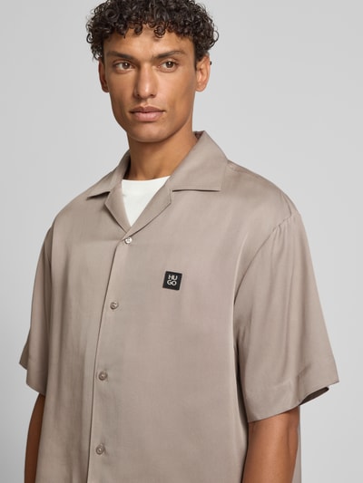Männermodel trägt Relaxed Fit Freizeithemd aus reinem Lyocell Modell 'ESPINO' von HUGO in unifarbenem Beige mit Logo-Patch, Nahaufnahme Oberkörper.